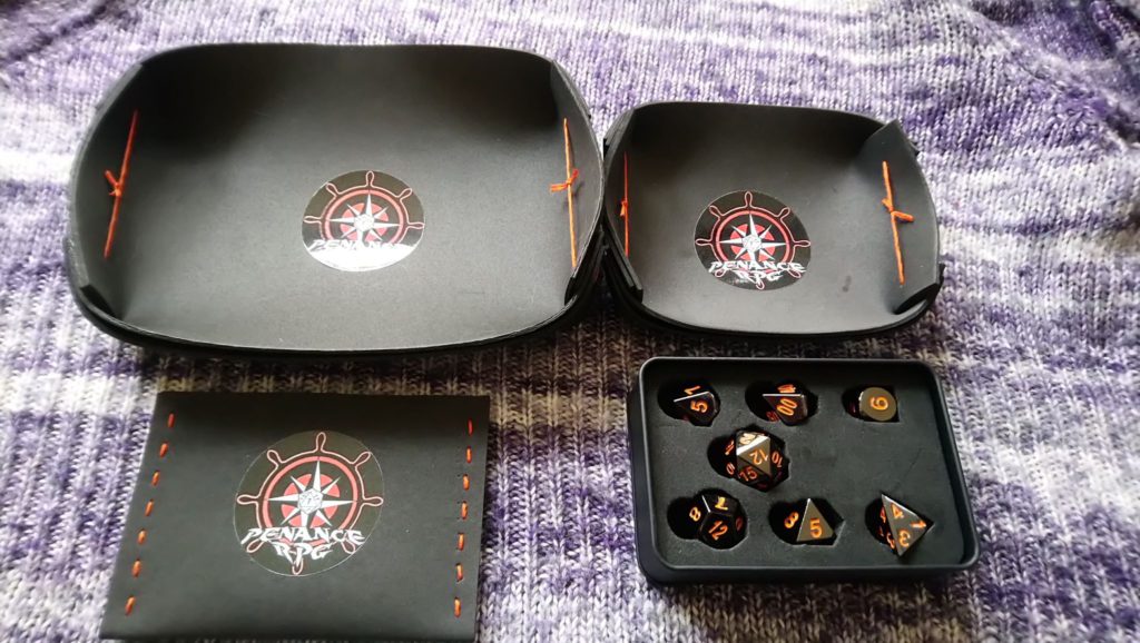 Black dice trays with orange seams with black metal dice .
Penance RPG, dice, metal dice, dice trays, black and orange