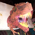 An open book with illustrations of dinosaur skull and a pop-up tyrannosaurus